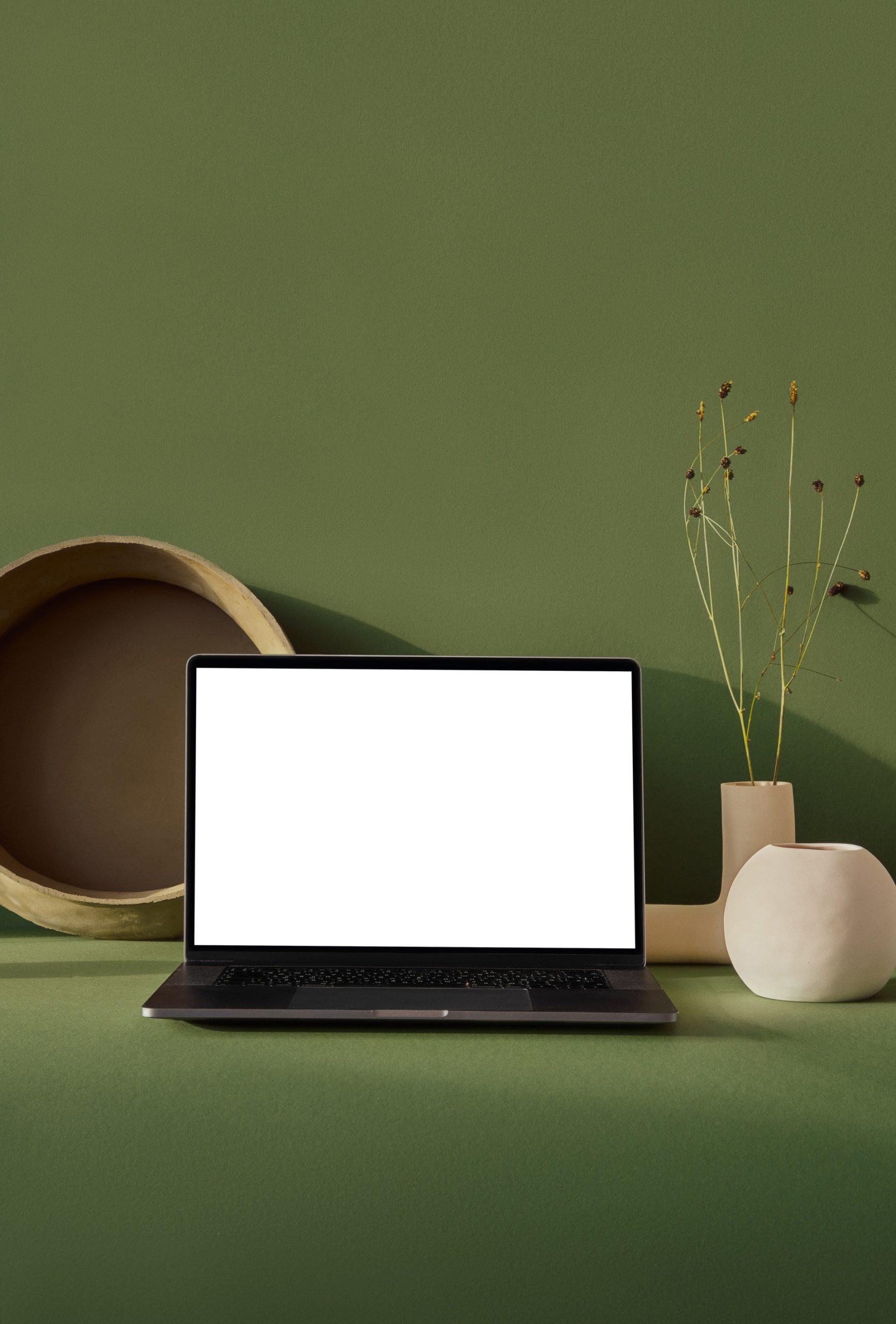 A laptop with a blank screen in front of a green wall.