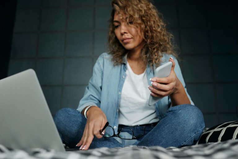 Woman reading off her computer while holding her phone.